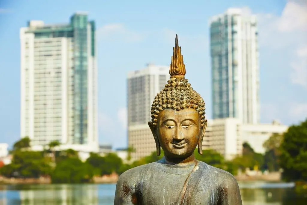 A bronze Buddha statue by the water with Colombo towers behind