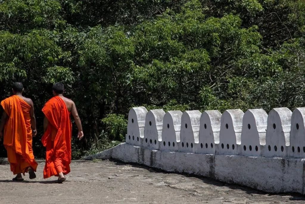Two monks in saffron robes walking beside a white temple wall