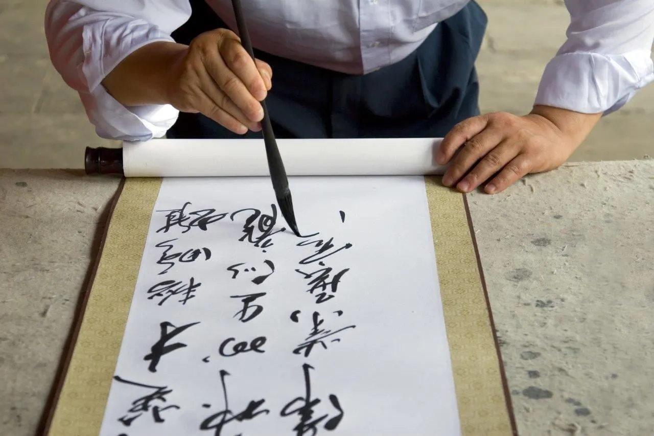 A brush writing Chinese calligraphy on a paper scroll