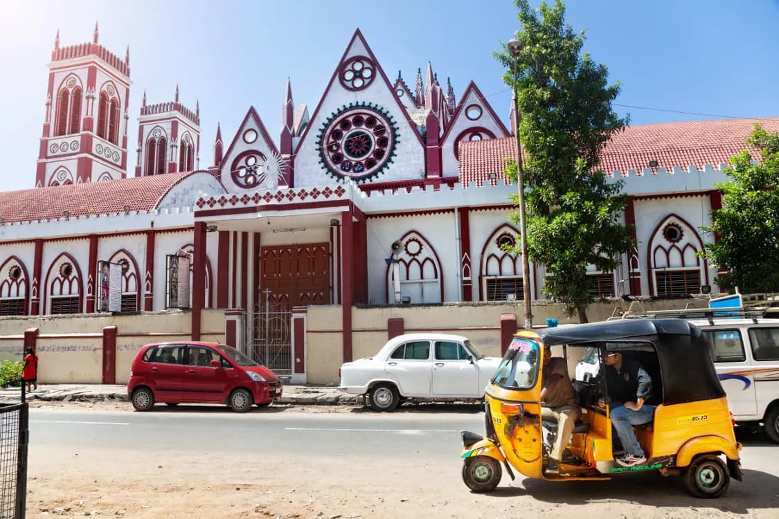 A red and white Gothic church with an auto rickshaw on the street outside