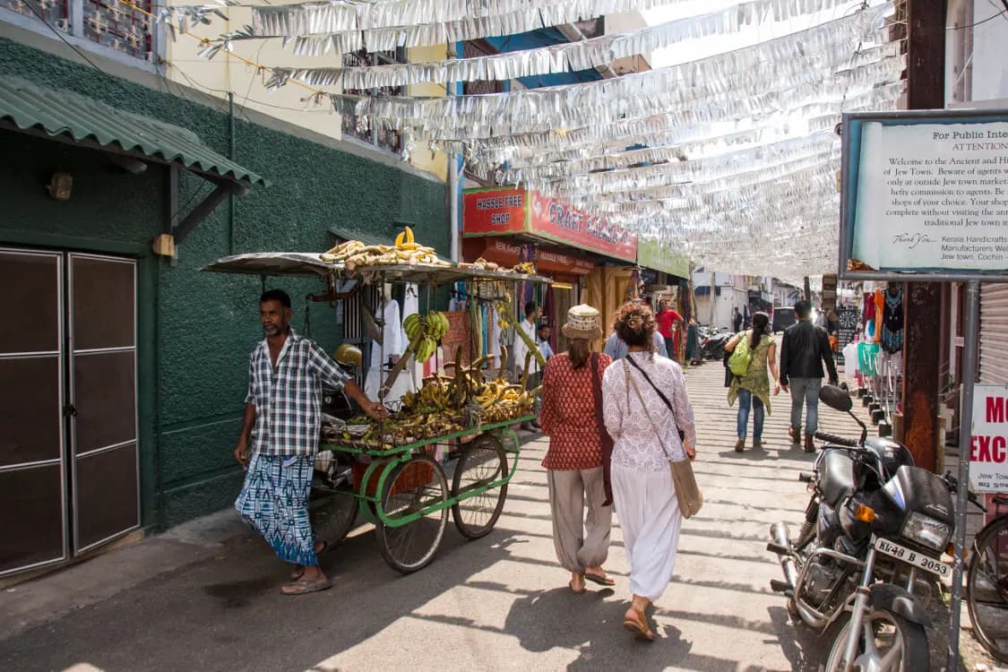 A street hung with silver bunting, with a fruit cart and people walking