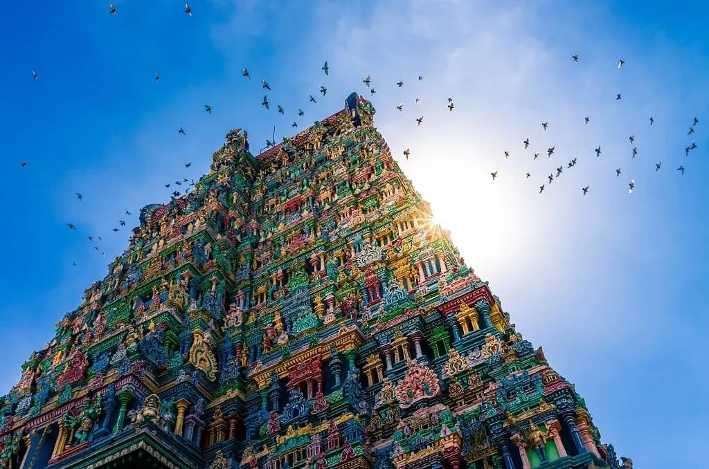 A painted temple gopuram lit by the sun, with birds circling overhead