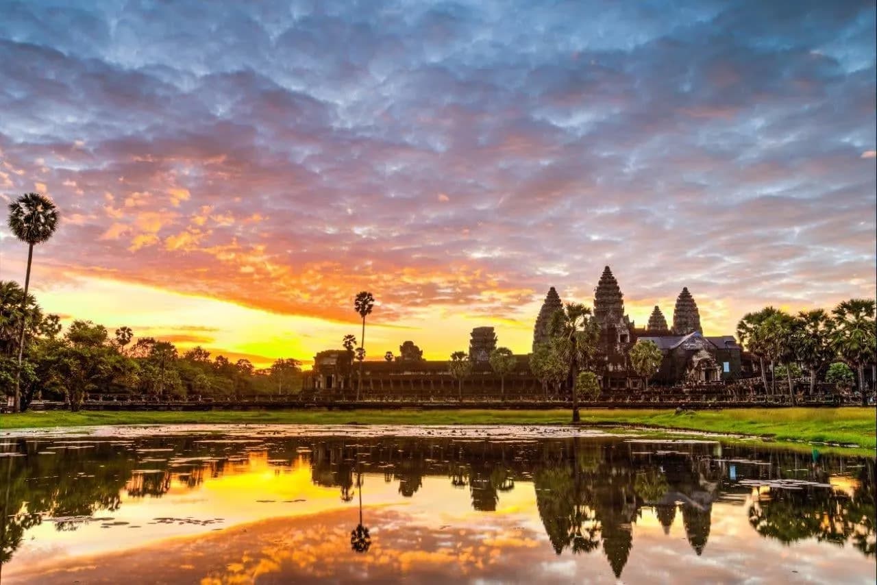 The towers of Angkor Wat reflected in a pond under a glowing sky