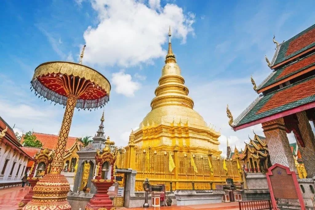 The golden chedi of Wat Phra That Hariphunchai in Lamphun, beside a tall ceremonial parasol