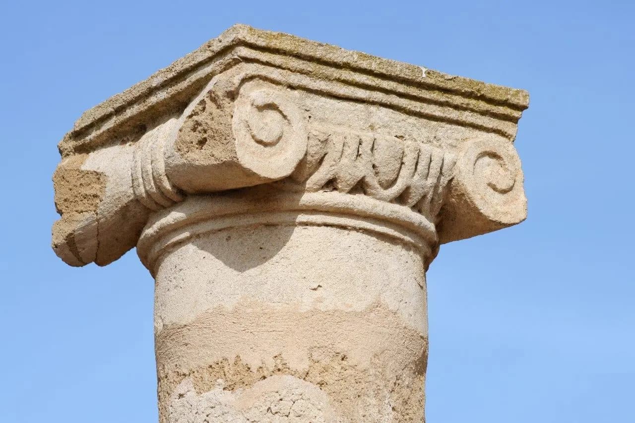 The carved capital of an ancient stone column against a blue sky