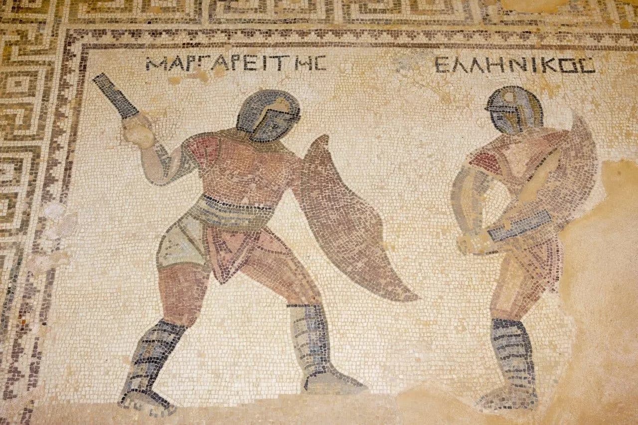 An ancient floor mosaic of two gladiators with Greek lettering