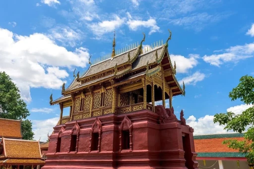 A red and gold Lanna-style temple pavilion under a bright sky
