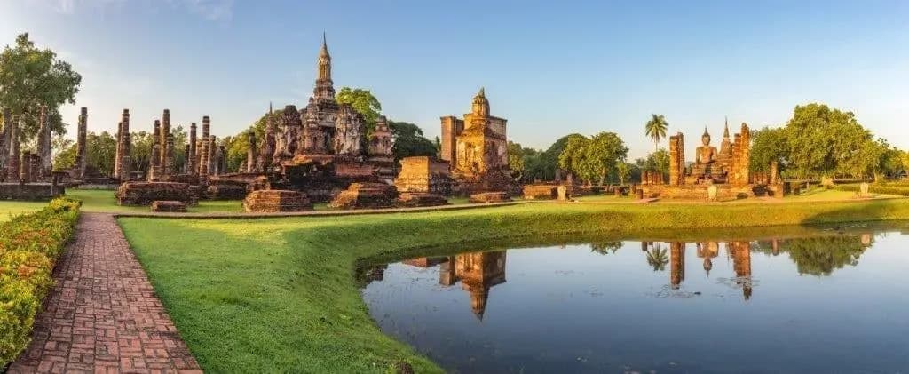 The chedis of Sukhothai's central temple ruins reflected in a still pond in late light