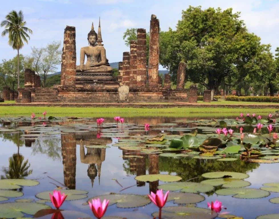 A seated Buddha at Wat Mahathat, Sukhothai, behind a lotus pond