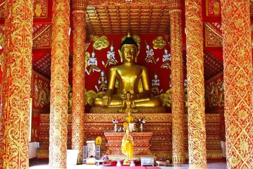A golden seated Buddha in a temple hall of red and gold pillars