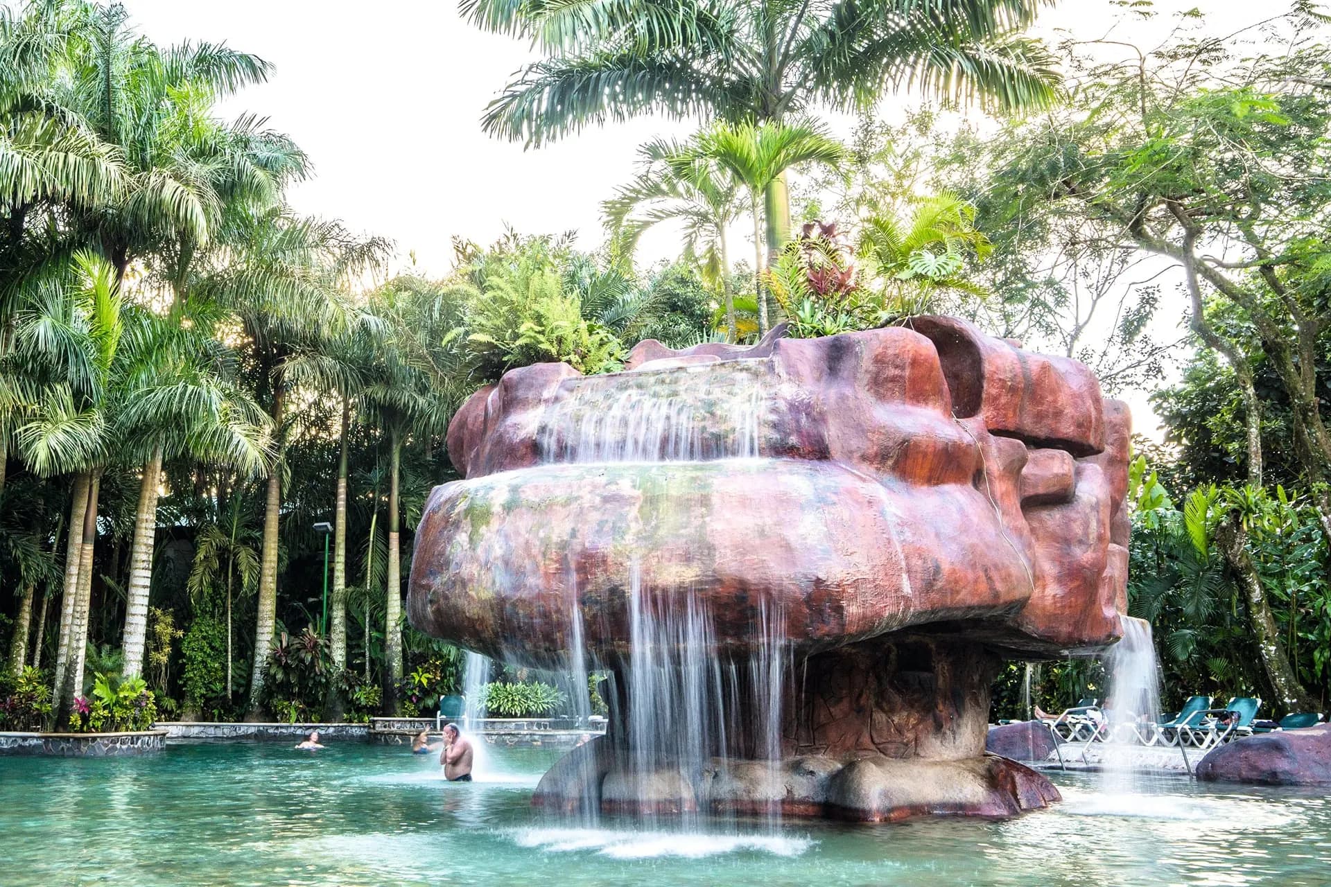 Warm water spilling from a rock fountain into a pool among palms