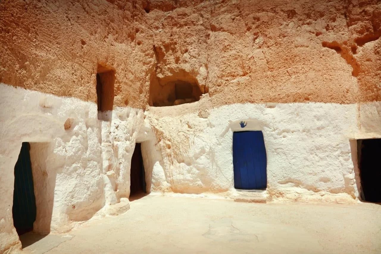 Whitewashed cave rooms with a blue door cut into a sandstone courtyard