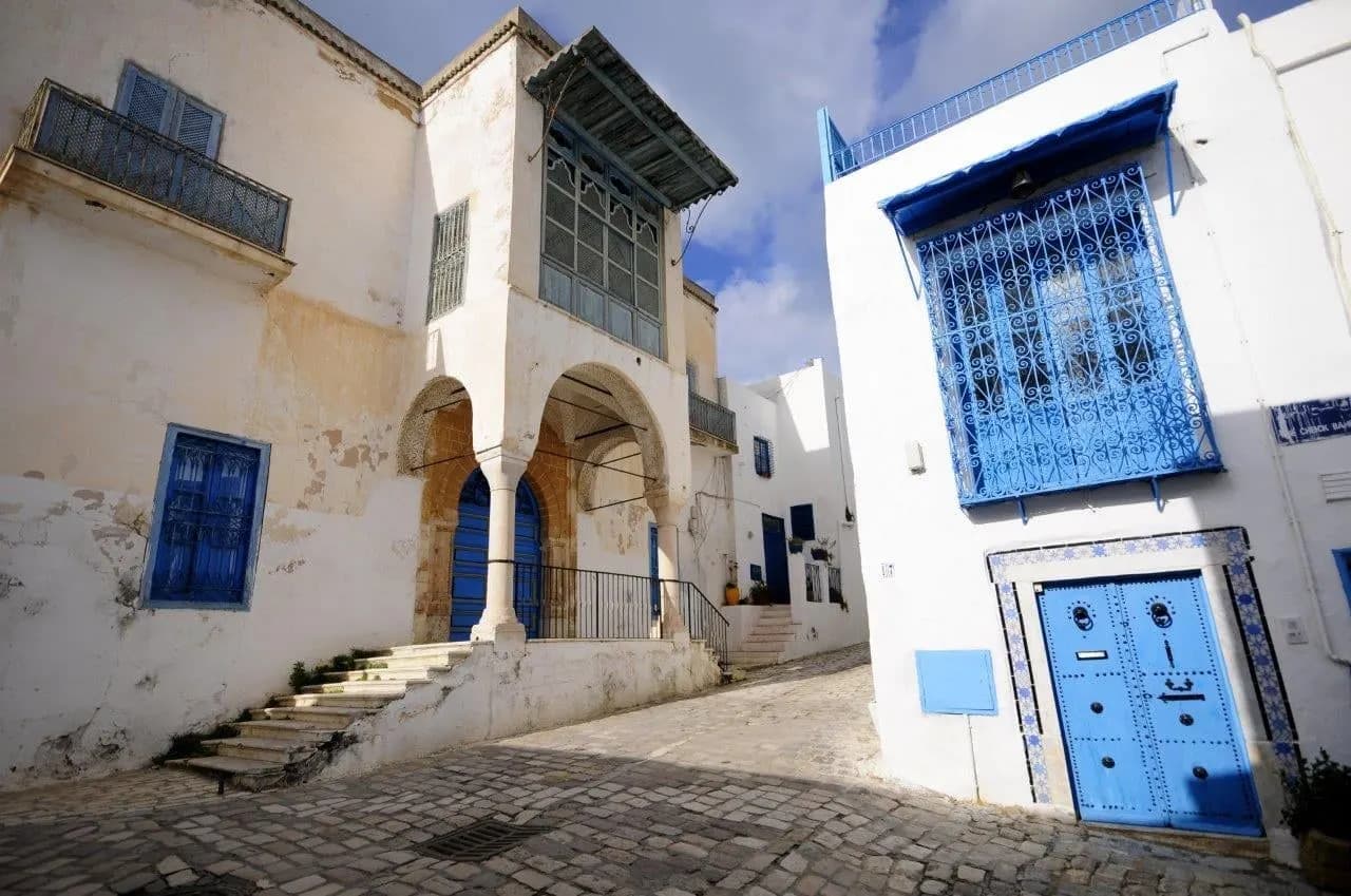 A cobbled lane of white houses with blue doors and shutters