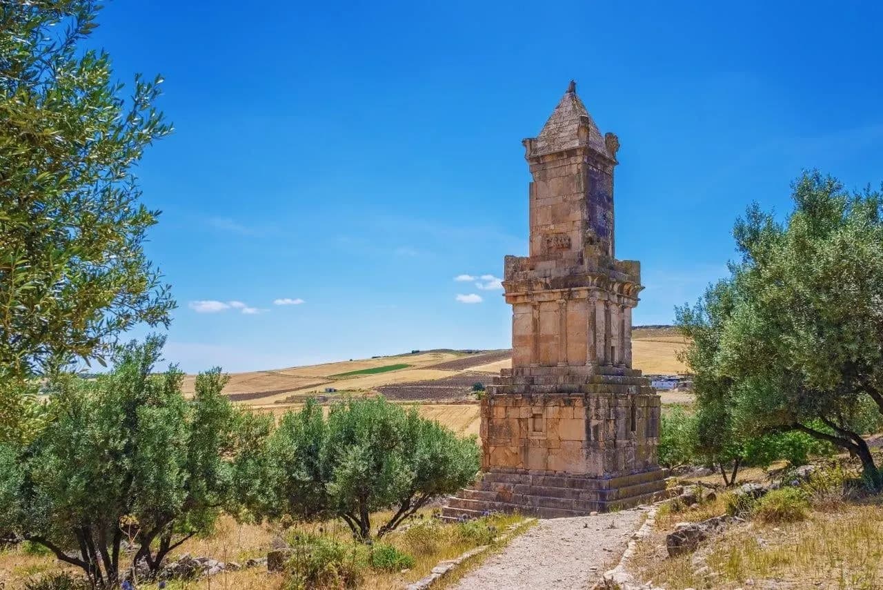A tall stone mausoleum among olive trees at Dougga