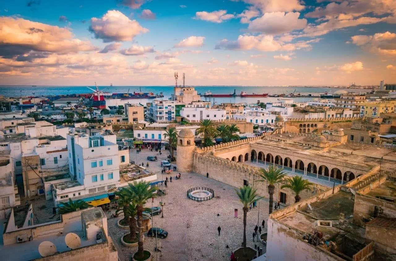 Whitewashed rooftops and a palm-lined square in an old Tunisian town at sunset