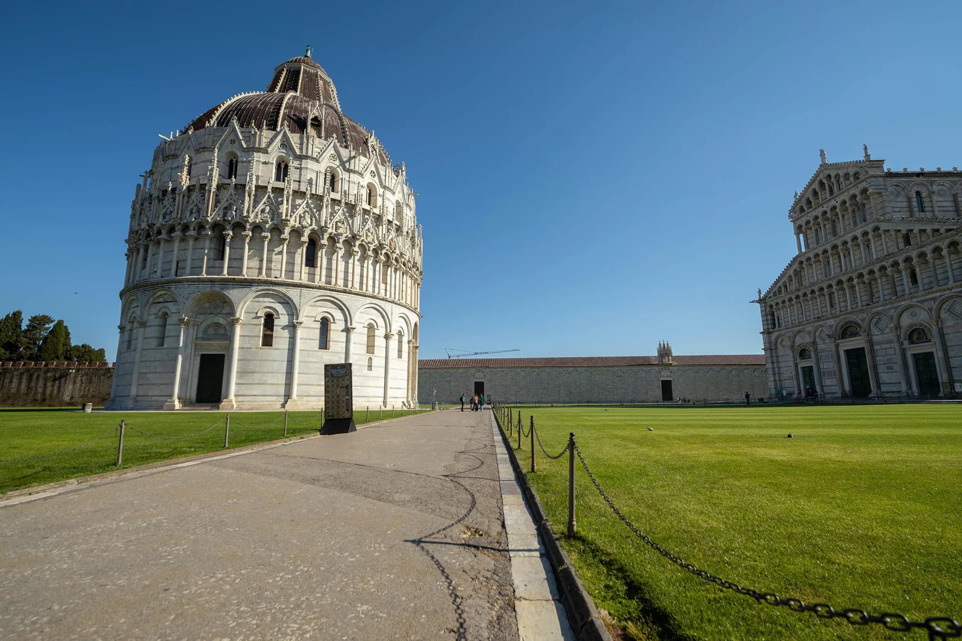 The round marble Baptistery of Pisa across green lawns from the cathedral