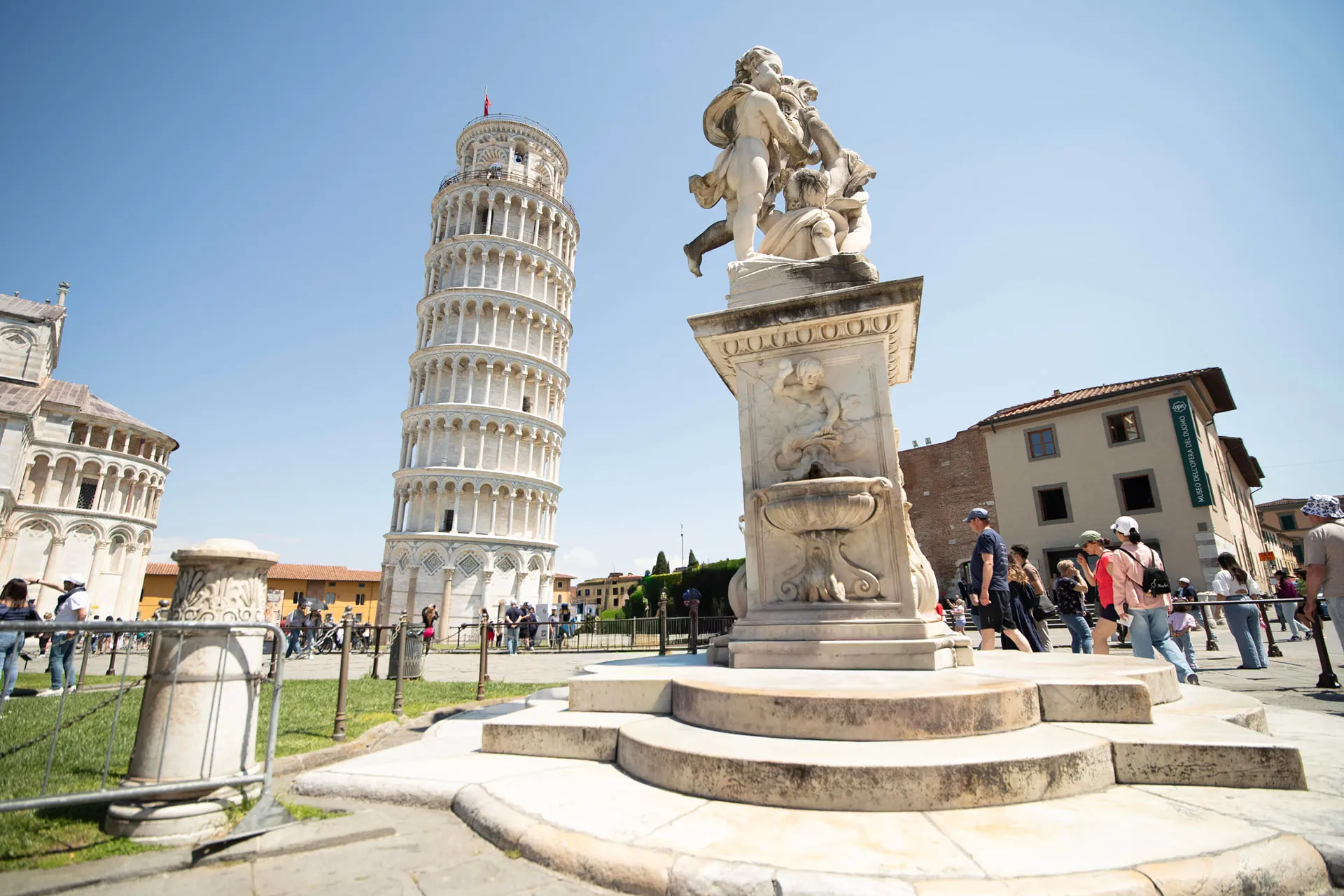 The Leaning Tower of Pisa beside a carved marble fountain in the Piazza dei Miracoli