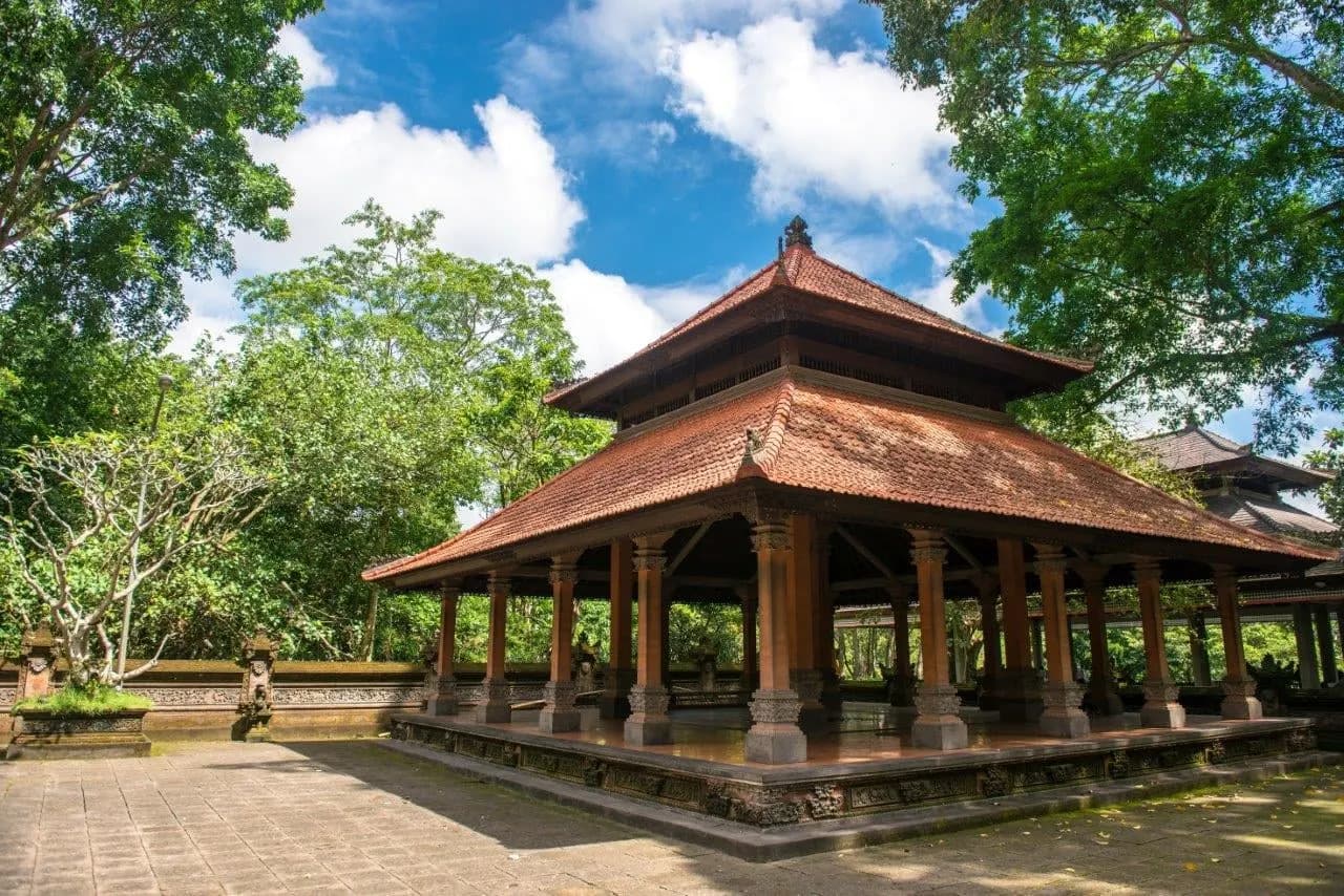 A wooden pavilion with a terracotta tiled roof in a shaded temple courtyard