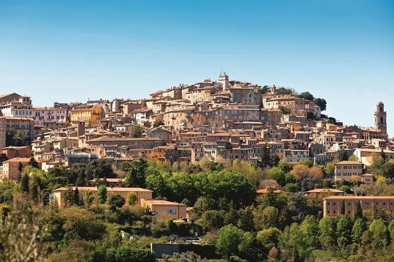 A medieval hill town crowning a green slope under a clear sky