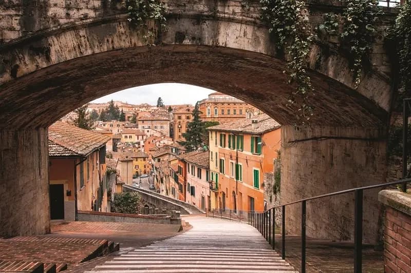A stone arch framing a stepped lane and terracotta houses in Perugia