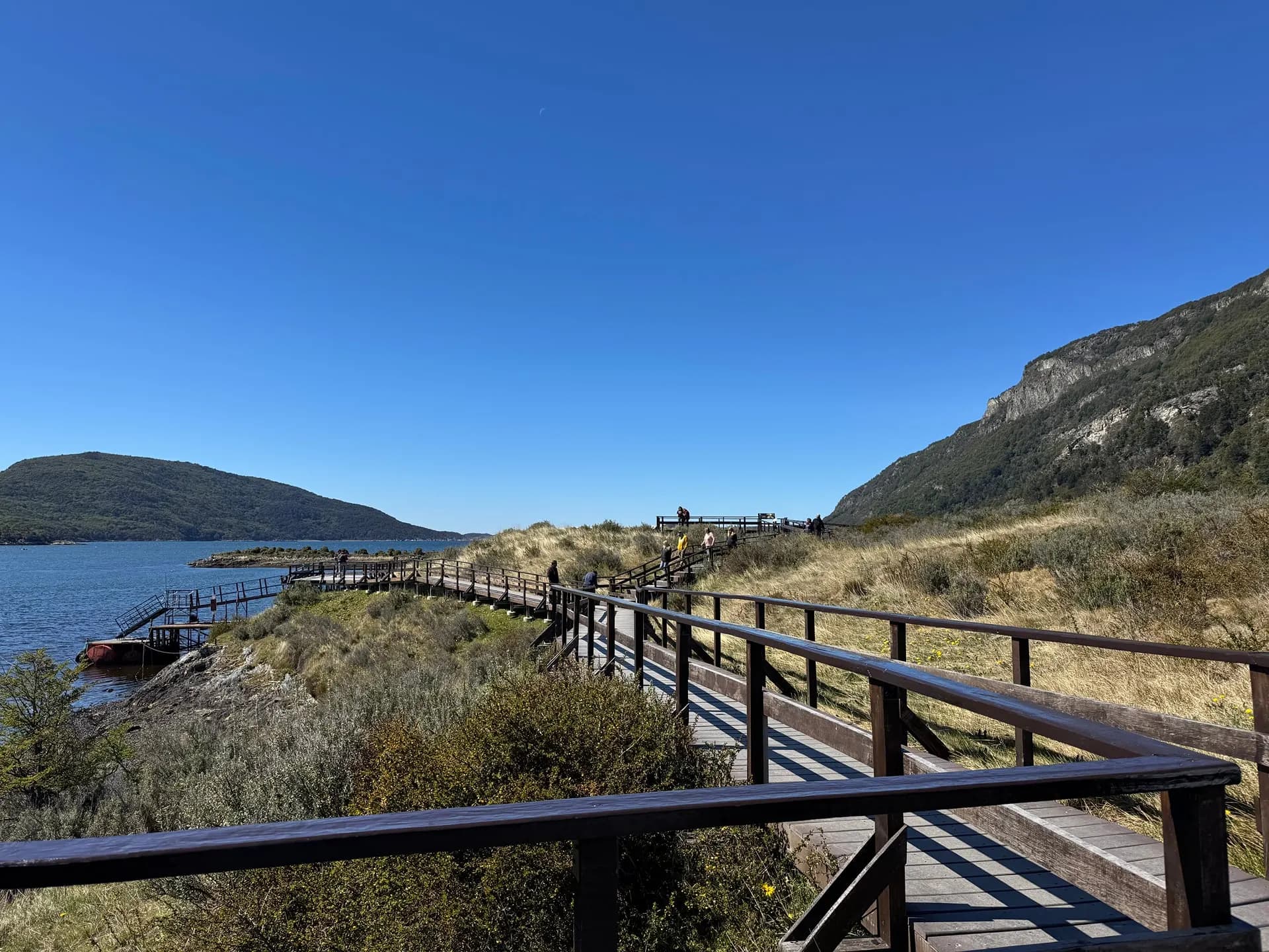 A boardwalk following the edge of a sunny bay below a rocky hillside