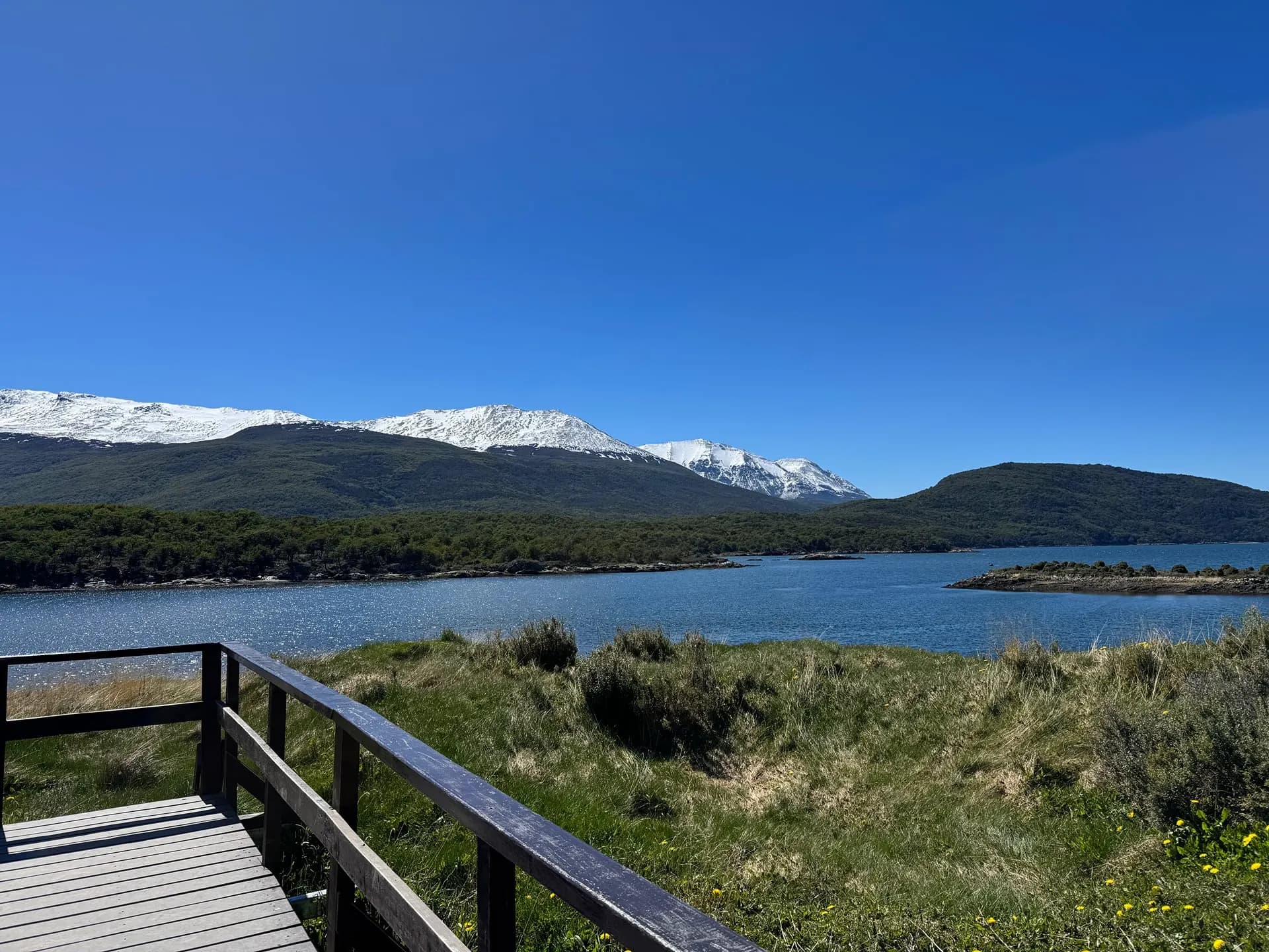 A wooden boardwalk above a bay with a long snowy mountain range beyond
