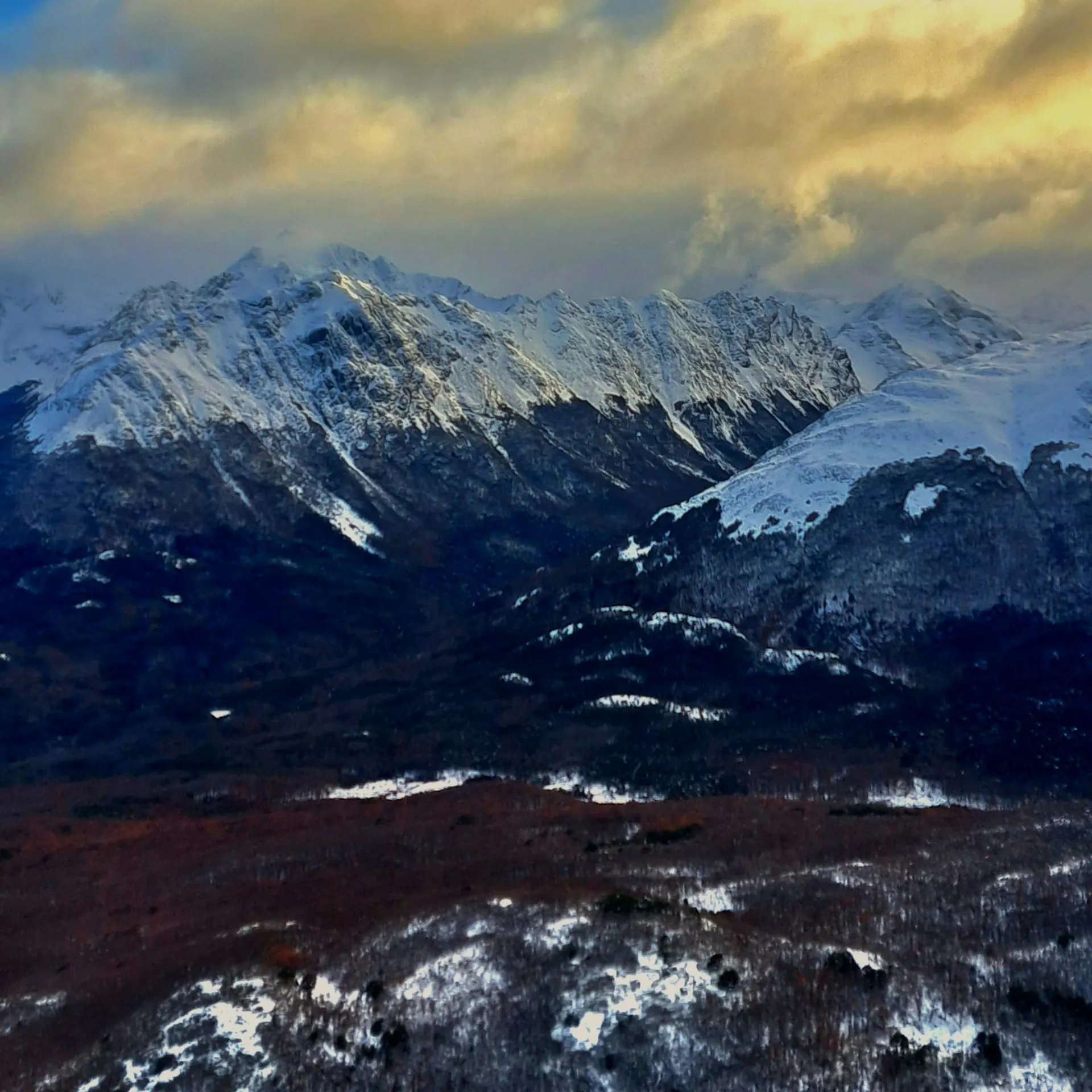 Jagged snow-covered mountains under golden evening cloud