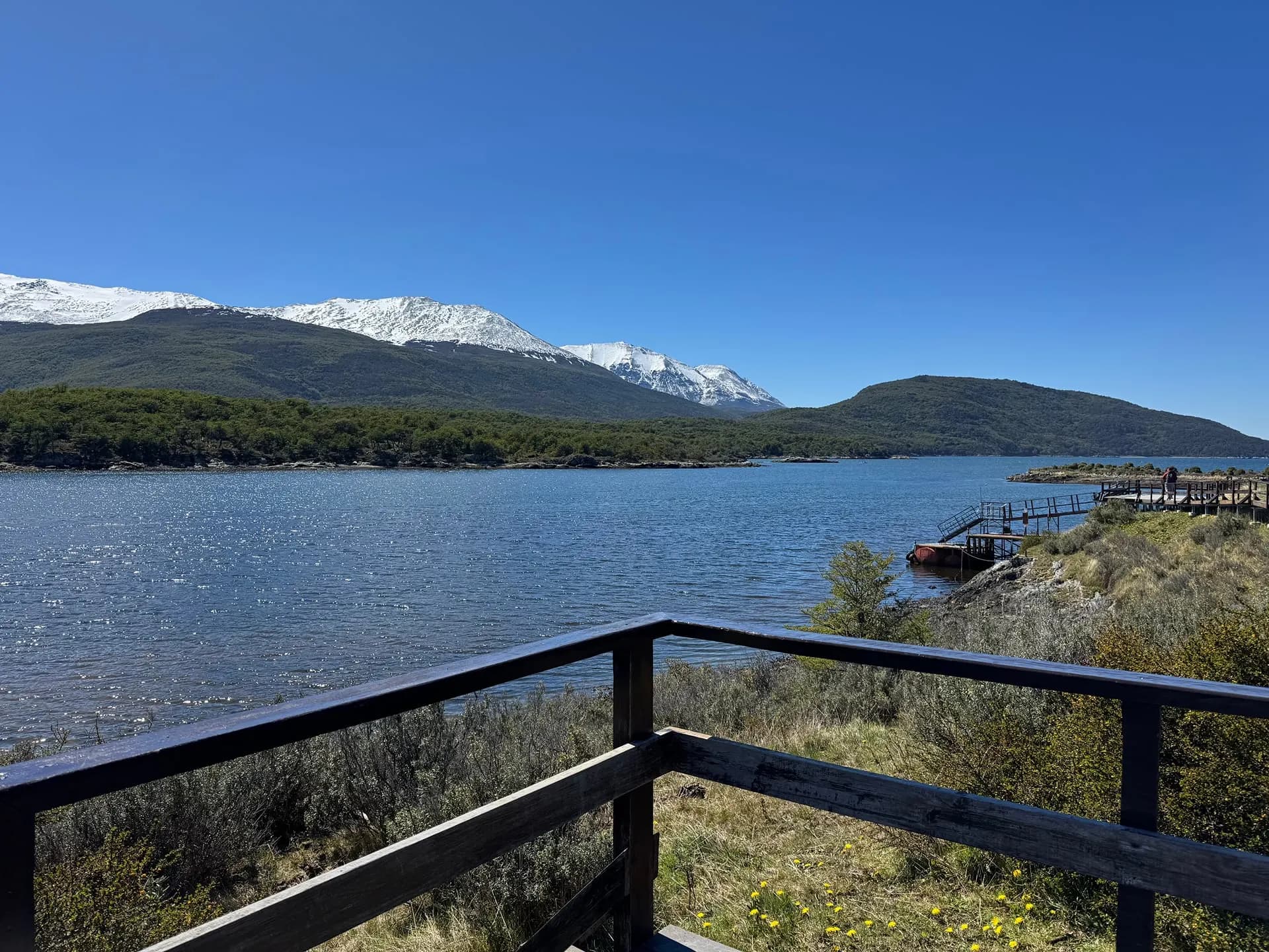 A lake framed by forest and snowy mountains, seen from a wooden viewpoint