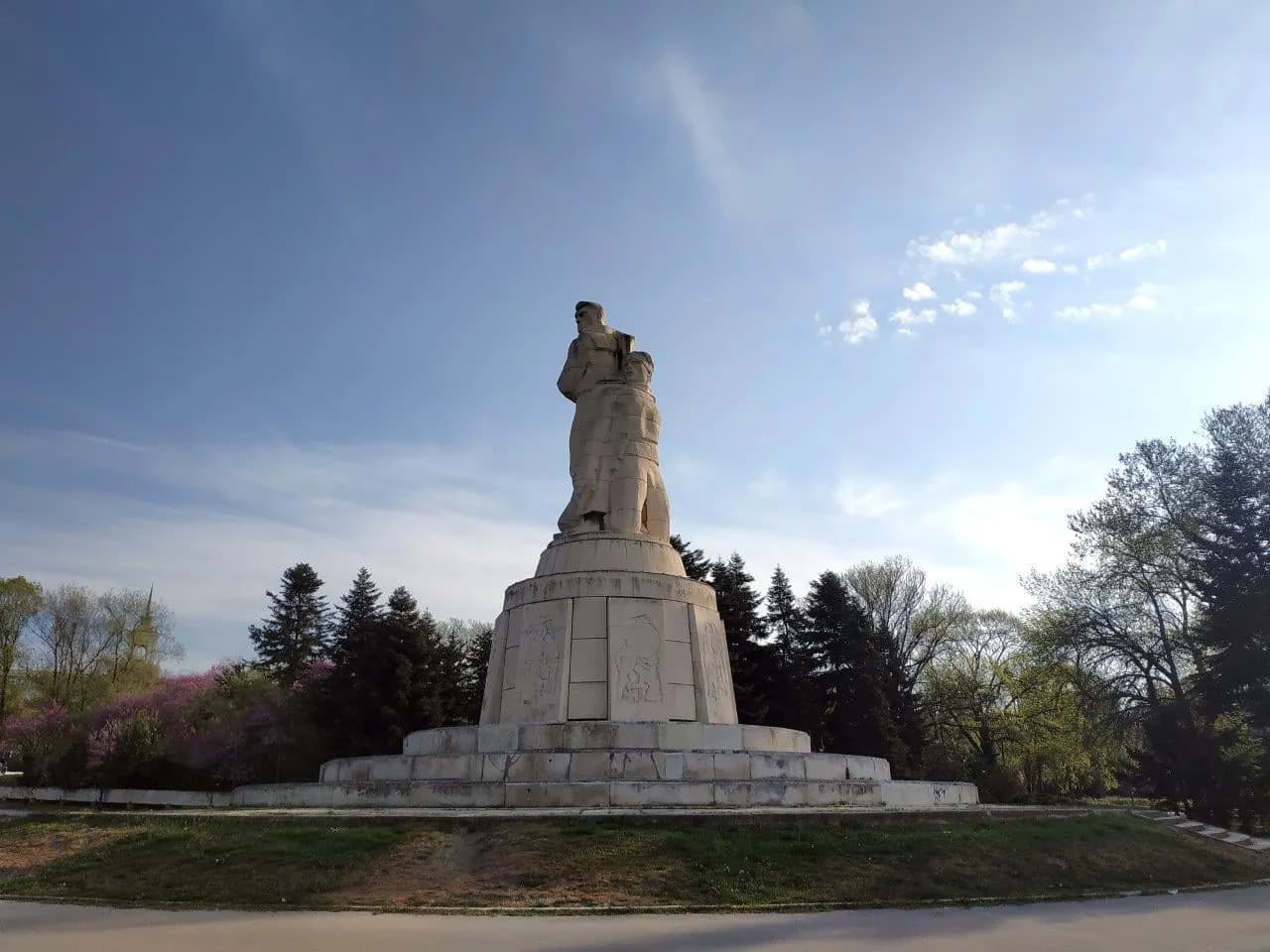 A large stone monument on a plinth above trees under a wide sky
