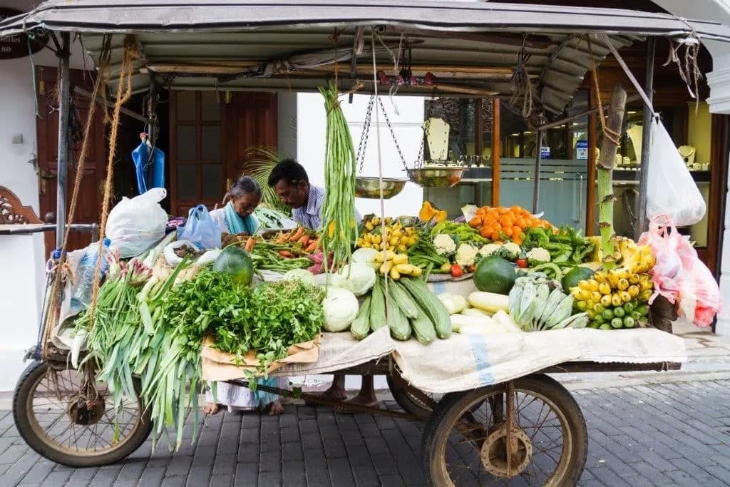 A street cart piled with fresh vegetables and bananas