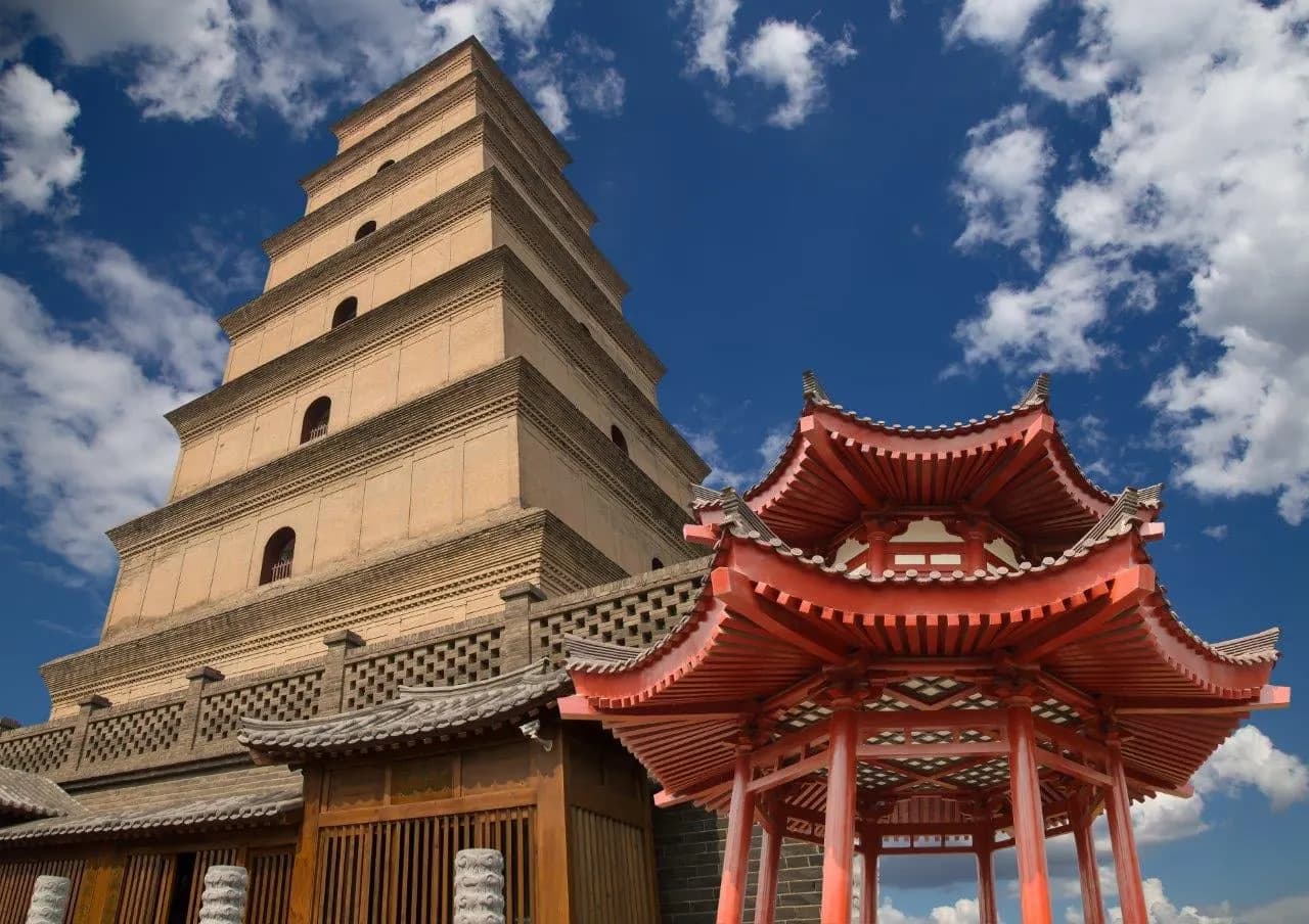 A tiered brick pagoda beside a red pavilion under a blue sky