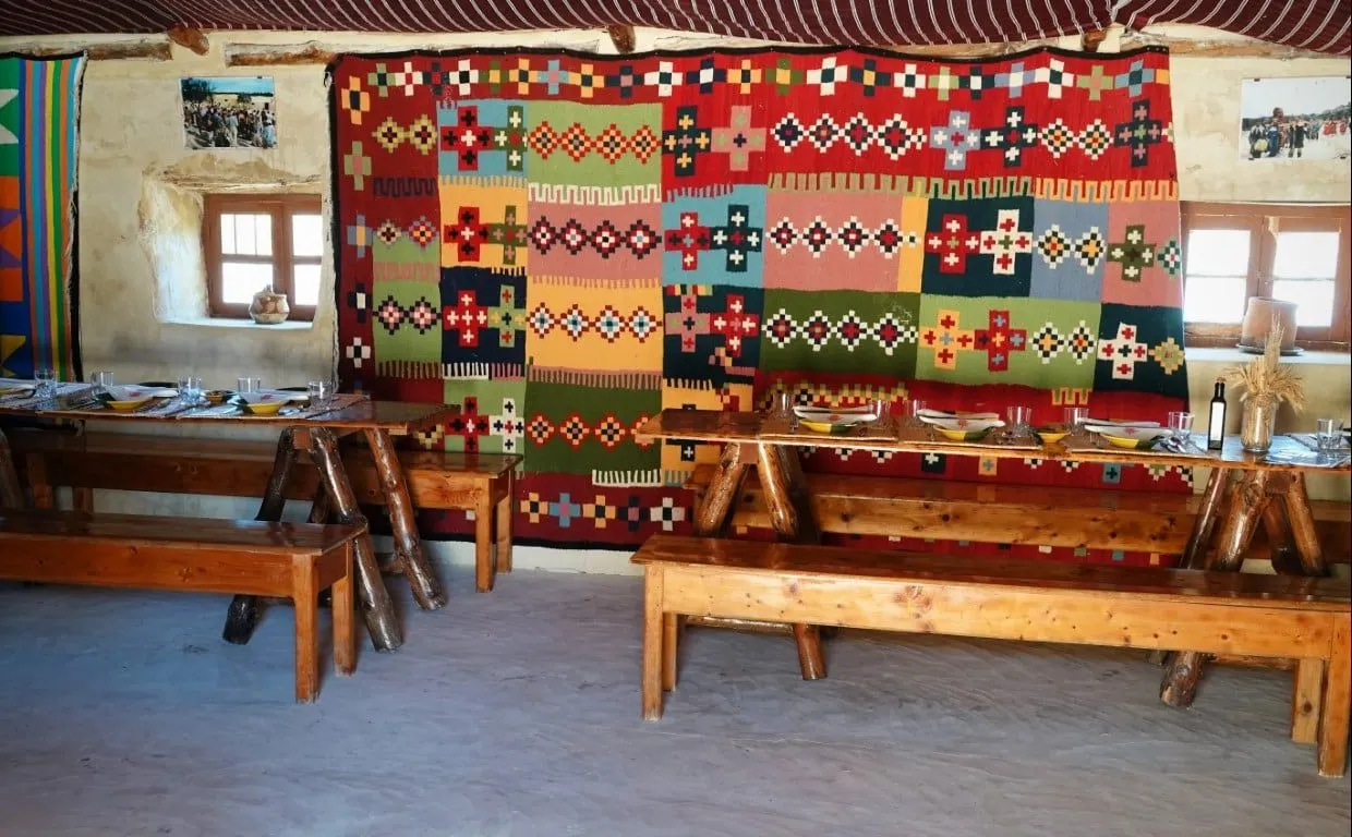 Long wooden tables beneath a bright woven kilim in a farm dining hall