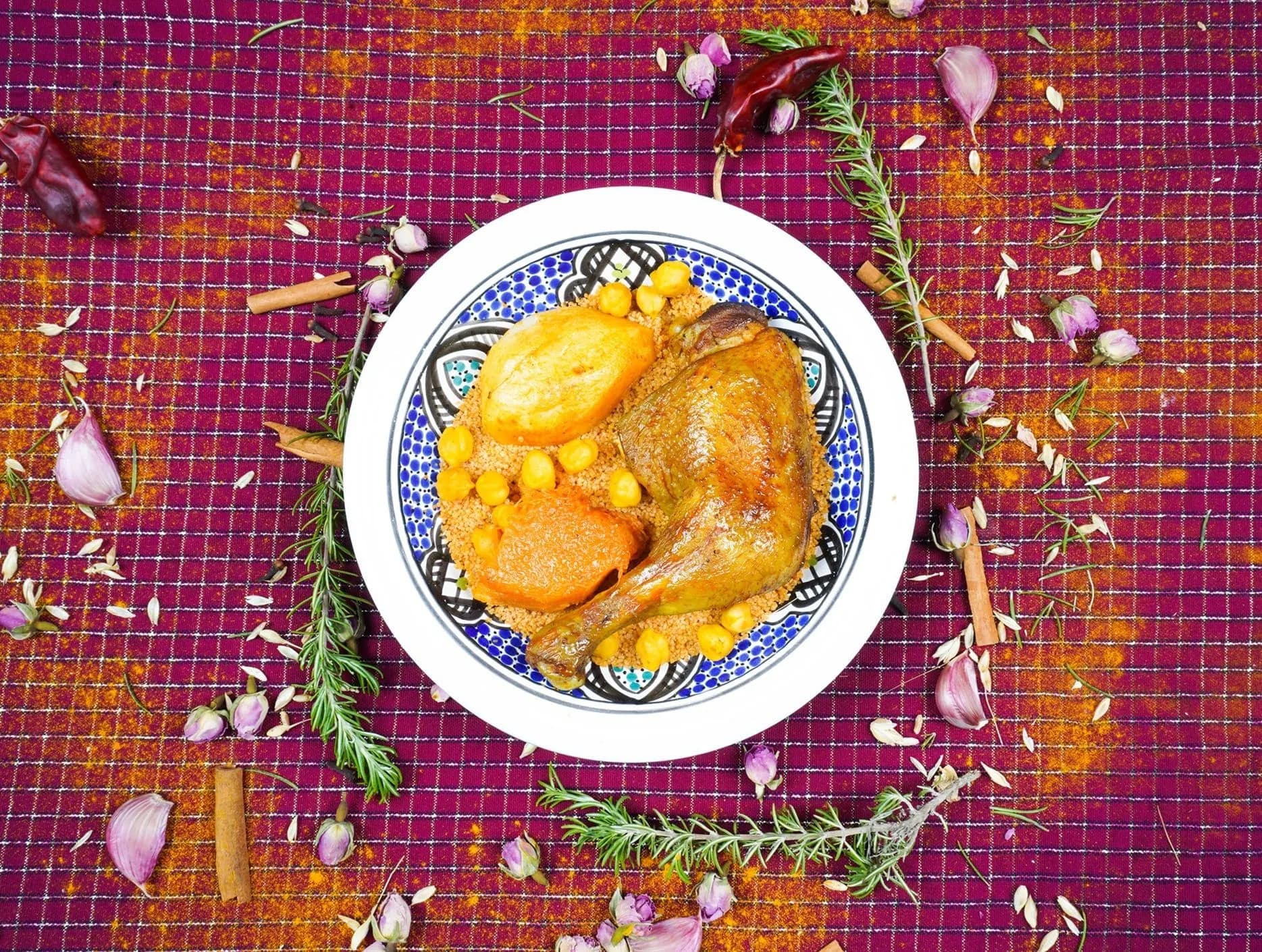 A Tunisian chicken and vegetable dish on a patterned plate scattered with herbs
