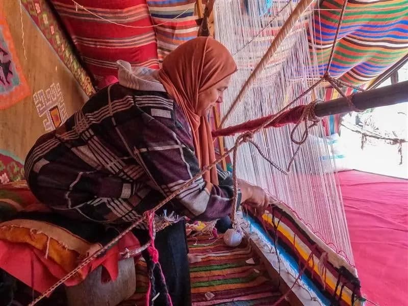 A woman weaving a striped rug at a wooden loom