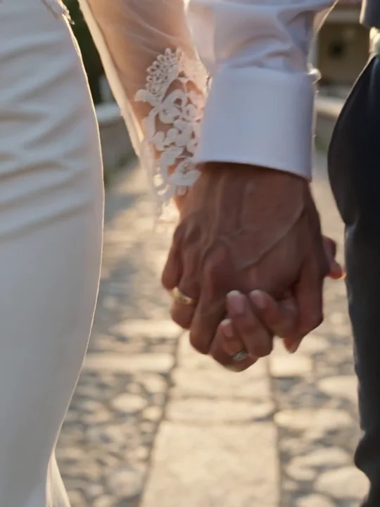 A bride and groom holding hands on a sunlit stone path