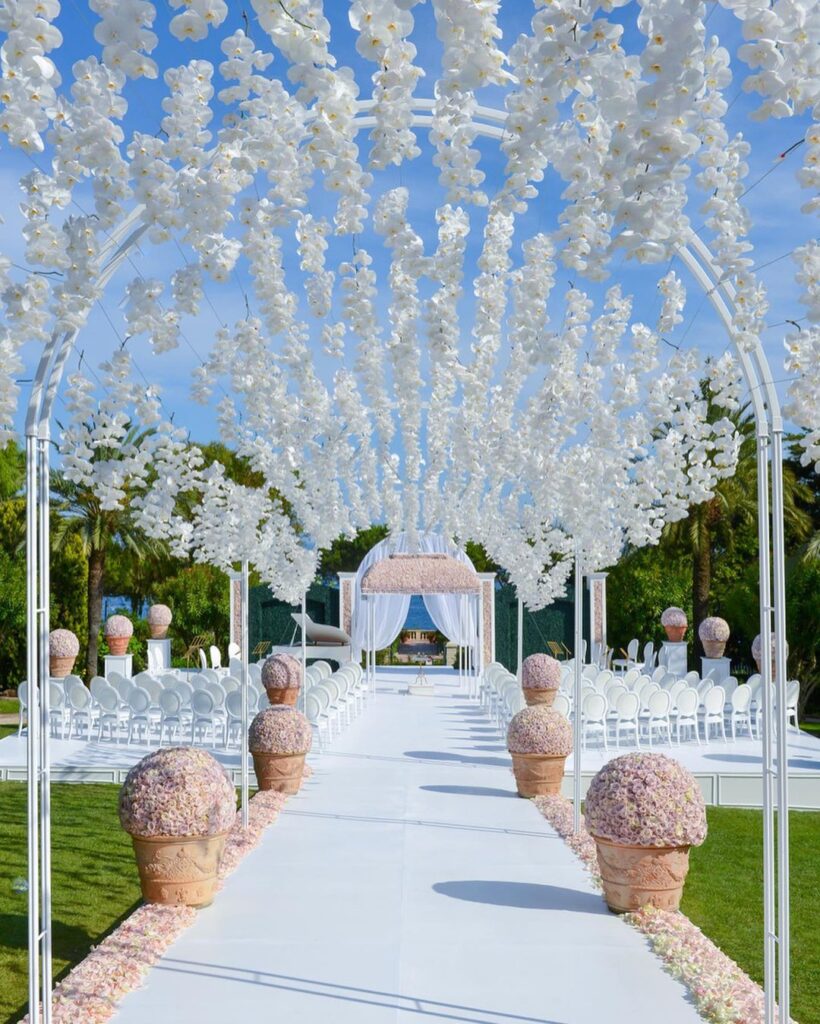 Breathtaking outdoor aisle with beautiful floral arches and pastel colored potted flowers.