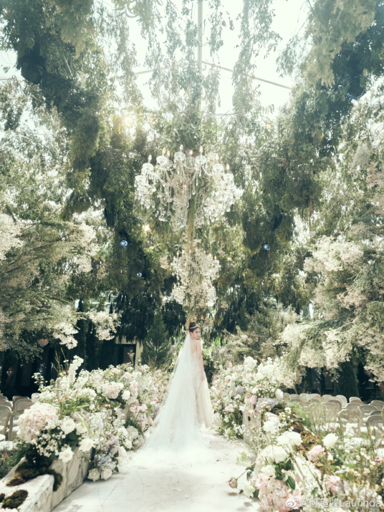 The stunning bride surrounded by lush greenery, beautiful florals, and elegant chandeliers.