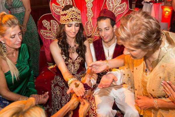 Bride and groom participating in Henna/Kina night, surrounded by family and friends, with traditional attire and henna application.
