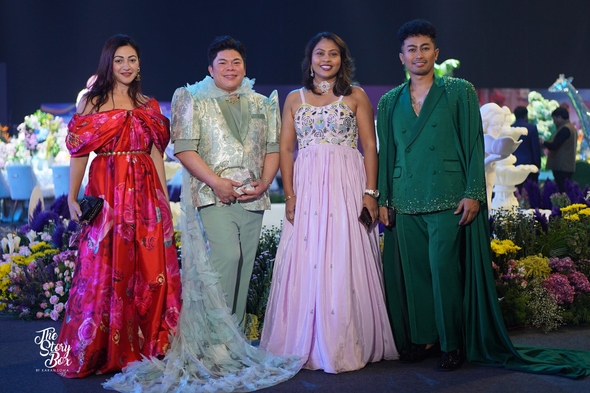 Group of four elegantly dressed individuals at a wedding event, showcasing vibrant fashion styles, with floral decorations in the background, reflecting the luxury wedding industry theme.