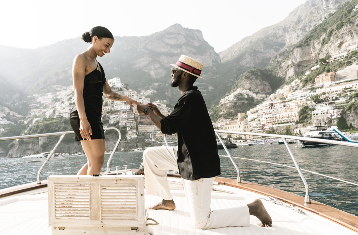 Couple on a boat in Italy, man proposing to woman, scenic coastal background, romantic destination wedding moment.
