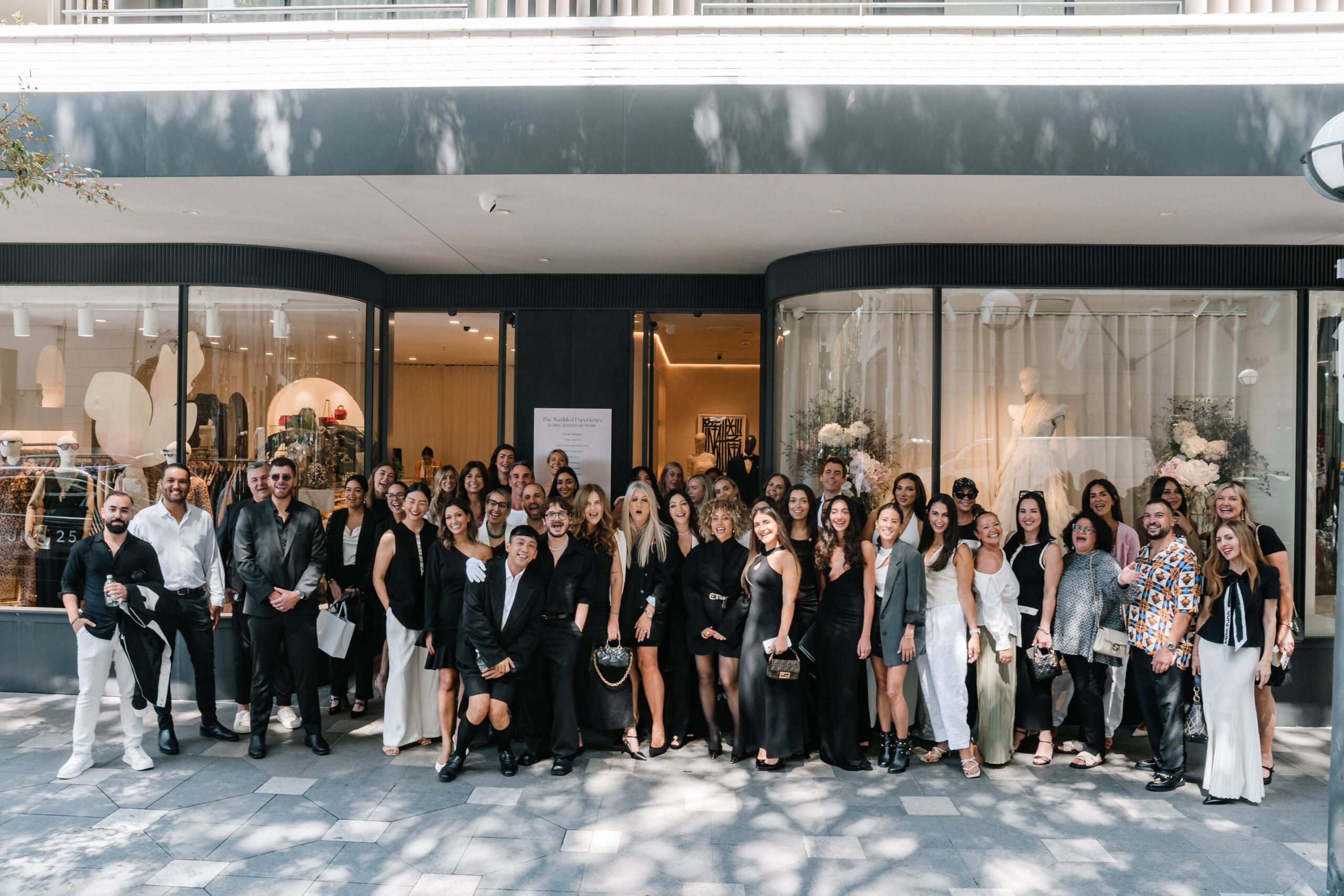 Group of wedding industry professionals posing outside a luxury bridal shop, showcasing a diverse crowd in elegant attire, celebrating the Wedded Network Sydney launch event.