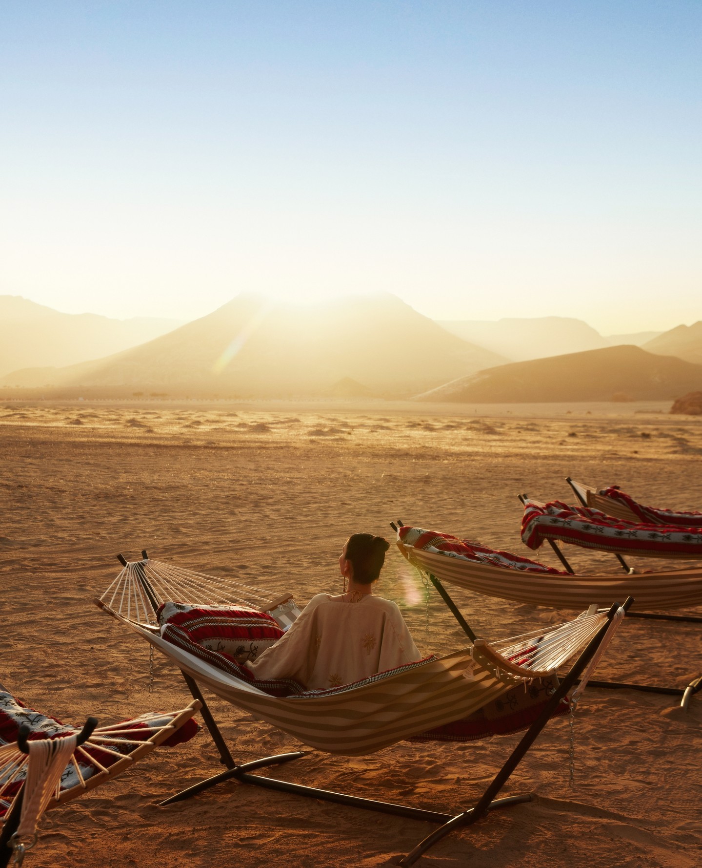 Woman relaxing in a hammock at a serene desert sunset, showcasing Middle Eastern wedding destination ambiance.