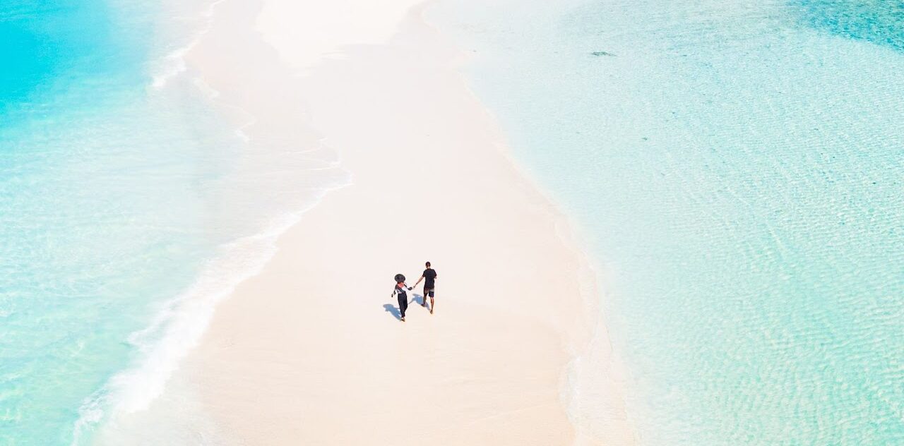 Couple walking hand-in-hand on a pristine beach, surrounded by turquoise waters, symbolizing romantic beach wedding destinations in Southeast Asia.