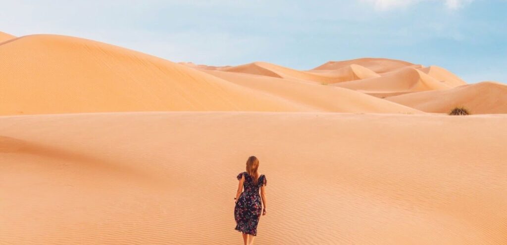Woman walking through golden sand dunes in the UAE, symbolizing a luxurious and adventurous honeymoon experience.