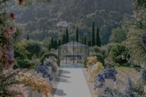 Elegant outdoor wedding venue with floral arrangements leading to a glass greenhouse, surrounded by lush greenery, ideal for destination weddings in Europe.