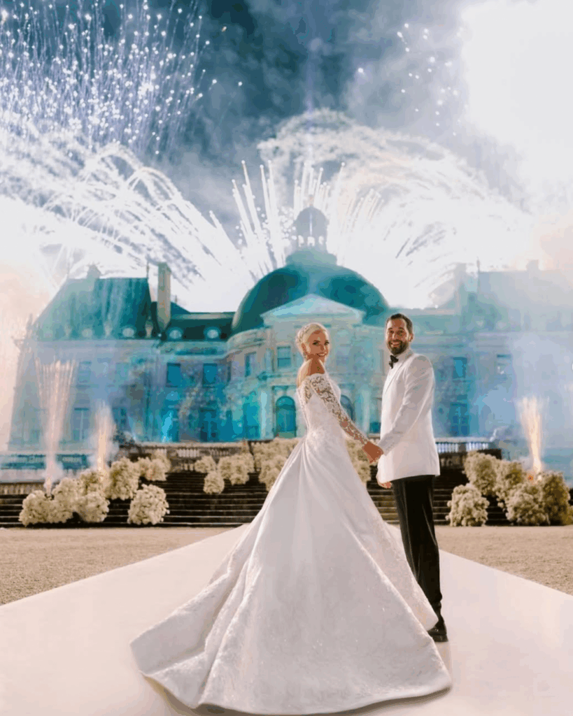 The Art of Extravagance: How Alejandra Poupel Creates Themed Events Like No Other 1 Couple in elegant wedding attire holding hands on a grand pathway, surrounded by fireworks and a lavish château, showcasing opulence and celebration.