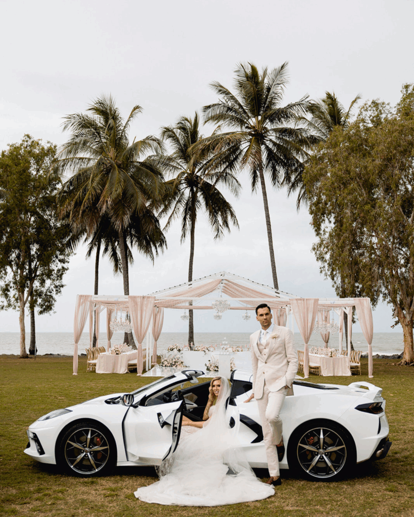 Where Sophistication Meets Storytelling: How Alysia Bridger brings love stories to life 9 Bride in elegant wedding dress sitting in a white sports car with groom in formal attire standing beside her, palm trees and a beautifully decorated wedding setup in the background, showcasing luxury wedding planning by Alysia Bridger Events.