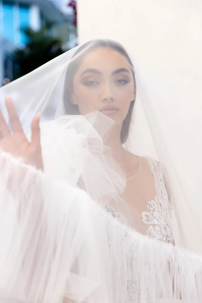 About Us 1 Bride in elegant wedding dress and veil, softly illuminated, showcasing intricate beading and lace details, embodying luxury and romance in a wedding setting.
