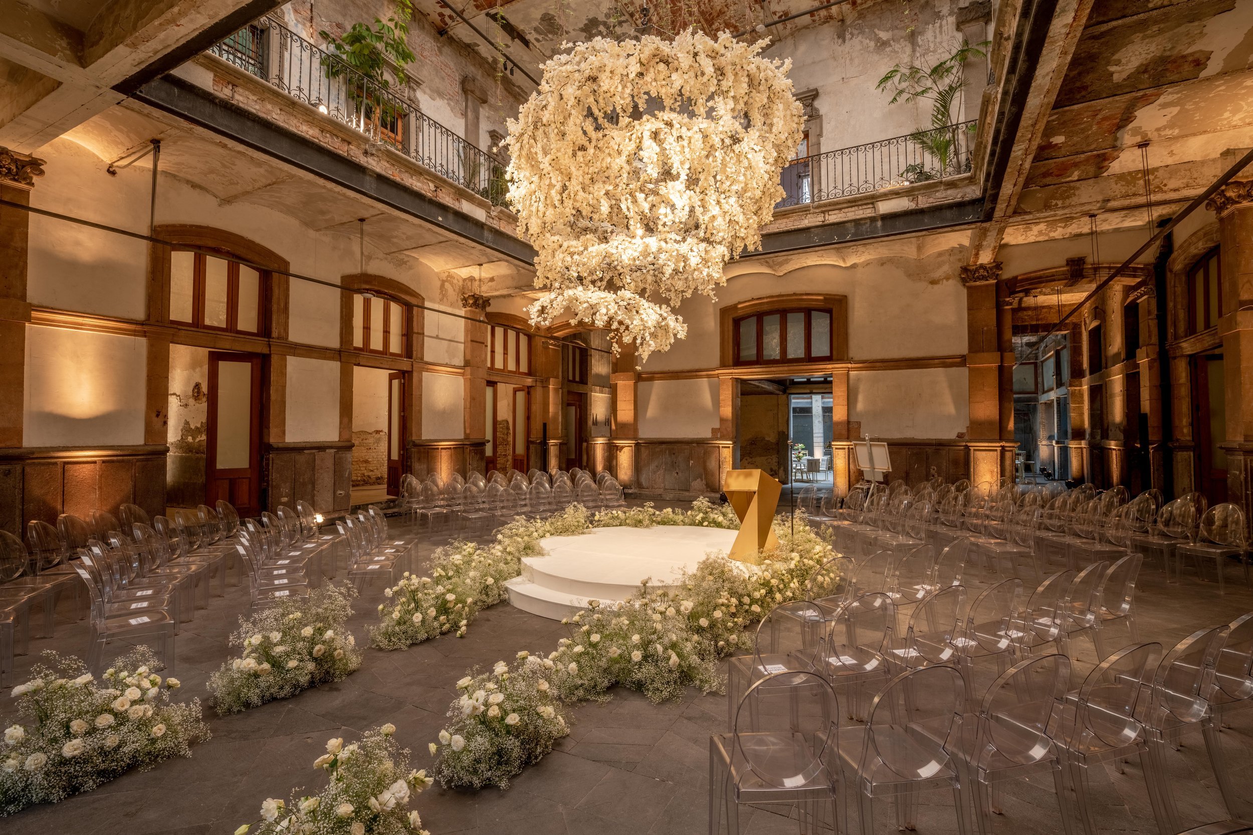 Elegant wedding ceremony setup in Mexico City featuring a floral chandelier, white floral arrangements, and transparent chairs surrounding a circular stage.
