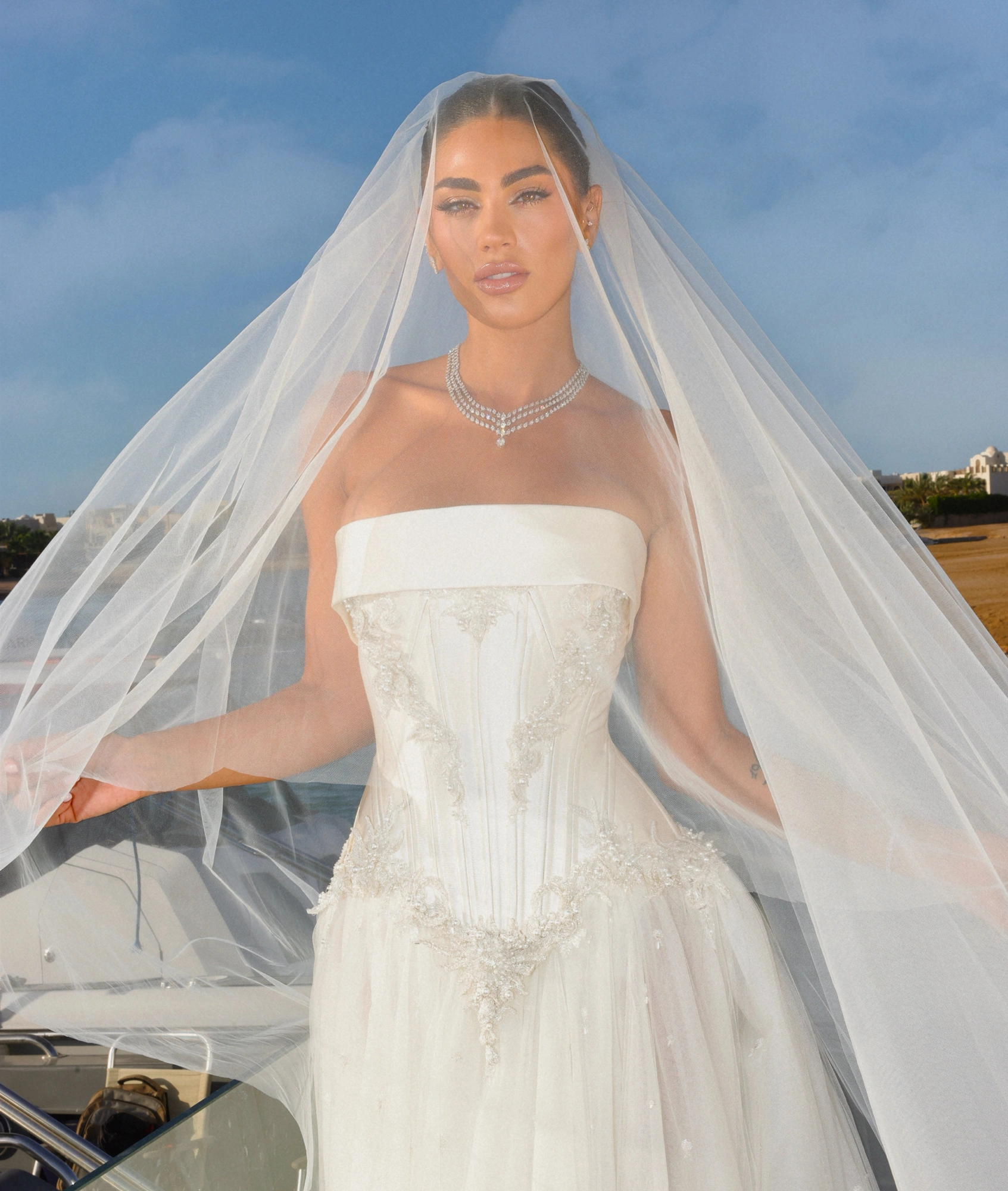 Bride in elegant strapless wedding gown with intricate detailing and flowing veil, set against a scenic outdoor backdrop, embodying luxury wedding inspiration for modern couples.